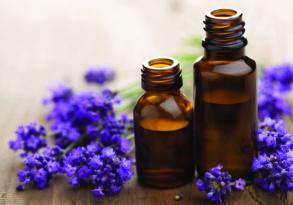 Two small amber glass bottles next to lavender flowers on a wooden surface, perfect for herbal bathing.