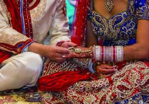 Bride and groom in traditional Indian attire performing a ritual during their wedding ceremony, exchanging rings under the influence of both Eastern love and Western influence.