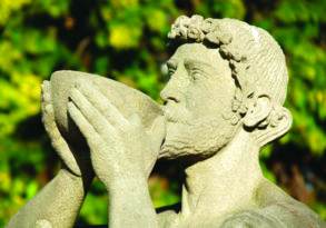 Stone statue of a man drinking from a bowl, surrounded by lush green foliage in the background, symbolizing the defense of intoxication.