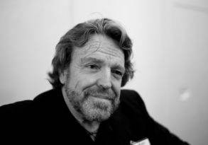 Black and white portrait of a smiling middle-aged man, John Perry Barlow, with a beard, looking directly at the camera.