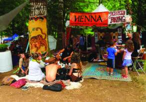 People experiencing bliss while visiting booths for henna and face painting at an outdoor festival with colorful decorations.