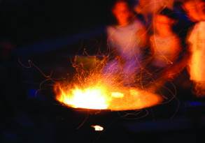 Blurred figures around a vibrant campfire at night, with dynamic sparks flying through the air, evoking summer memories.