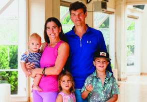 A family of five, including a couple and three young children, smiling together in a bright indoor space after experiencing the health benefits of yoga.