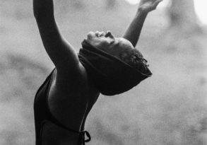 A woman in a misty forest, arms raised, head tilted back in a gesture of liberation or joy. Black and white photo.