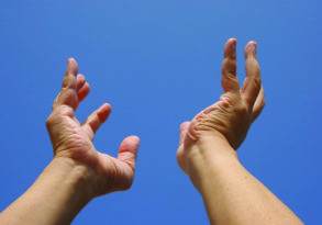 Two hands reach upwards against a clear blue sky, palms open with fingers slightly curved, as if capturing the essence of last words spoken softly to the heavens.