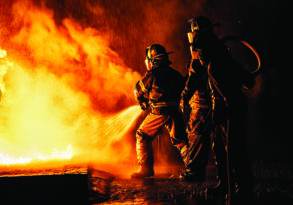 Firefighters in protective gear use a hose to douse flames in a night-time fire incident titled "Everything Is Burning.