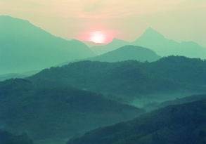 Group of people sitting on a hilltop, watching the sunrise over a mountain range during their first trip to India.