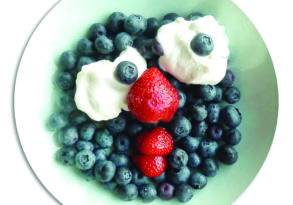 A plate of blueberries and strawberries topped with dollops of whipped cream, each topped with a single berry, inviting enjoyment of food.