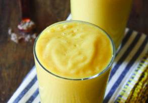 Two glasses of mango lassi on a striped napkin with a whole mango and cinnamon stick in the background at a coffee shop.