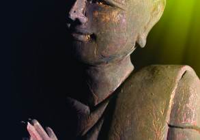 Sculpture of a seated Egyptian scribe, detailed with visible facial contours and traditional posture, highlighted by a greenish-brown lighting effect that invokes a sense of spiritual growth.