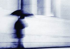 Blurred image of a person walking with an umbrella near building columns, conveying a sense of loneliness and motion in a monochromatic blue tone.