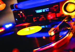 A turntable playing a vinyl record with vivid blue and red lighting, alongside a speaker and audio equipment in the background.