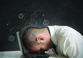 A man in a white shirt resting his head on a laptop, with illustrated gears and swirls around his head against a blackboard background, symbolizing his struggle to overcome fear of failure.