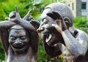 Bronze statues of two exaggerated figures practicing laughter yoga, with one holding its head and the other making a playful gesture with its hands, surrounded by palm trees.