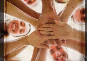 Overhead view of a group of smiling people stacking hands in a gesture of teamwork and unity, symbolizing the force of collaboration.