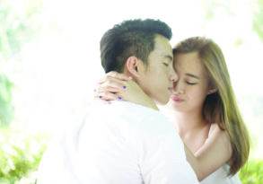 A couple embracing lovingly in a soft-focus natural setting, with the man kissing the woman's forehead.