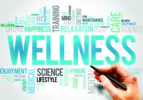 A hand with a pen adds to a colorful word cloud centered around the word "wellness," featuring related terms like "health," "fitness," and "What's in a Name?"