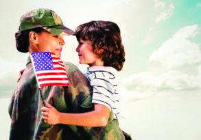 A young child in a striped shirt holding a small American flag embraces a smiling female veteran in military uniform, under a cloudy sky.