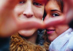 A couple forming a heart shape with their hands, framing their smiling faces, against a blurred background, embodying an authentic connection.