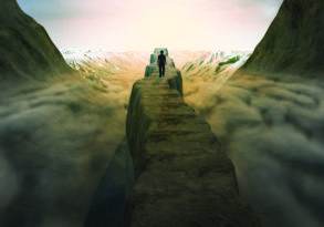 A person stands on a narrow rocky path between steep cliffs, embodying personal growth as they face a sunset over snow-capped mountains in the distance.