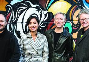 Four adults smiling, standing in front of a colorful graffiti wall. Two men and a woman, all members of the Kronos String Quartet, wearing casual outfits.