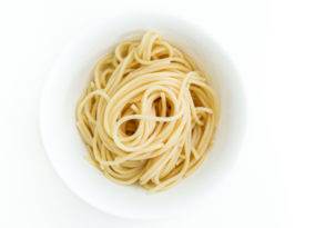 Plain cooked spaghetti noodles served in a white bowl on a white background.