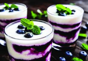 Three glasses of layered blueberry dessert featuring probiotics, topped with fresh blueberries and mint leaves on a wooden table.