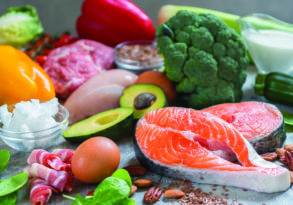 Assorted ketogenic diet foods including vegetables, low-carb fruits, nuts, meats, and fish on a kitchen counter.