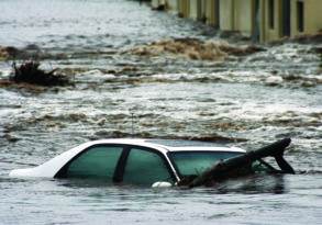 A submerged car in floodwaters with debris floating nearby, indicating severe flooding and hinting at the last words of an unseen tragedy.