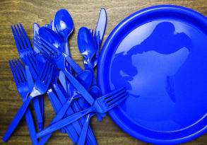 A collection of blue plastic cutlery and a plate with a map outline on a wooden surface, highlighting the environmental impact of plastic waste.