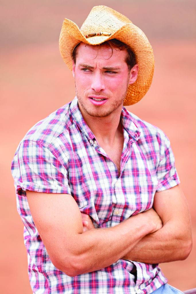 Cowboy man handsome and good looking with hat in rural USA countryside. Male model in american western prairie landscape nature on ranch or farm in USA.