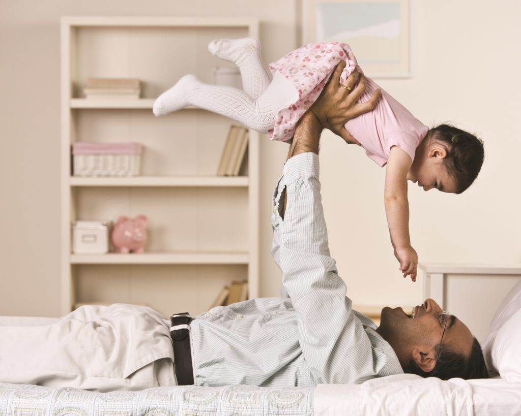 father lies on the bed and lifts his daughter into the air