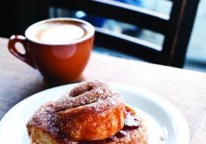 A freshly baked sugar-coated pastry on a white plate next to a red cup of coffee on a wooden table by a window in a timeless eatery.