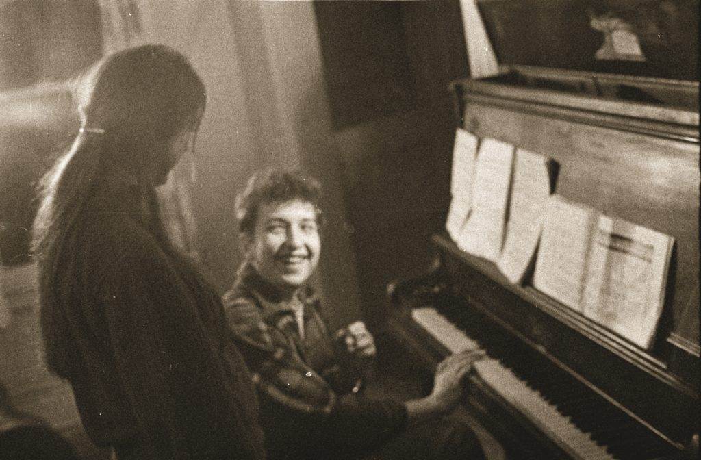 Bob Dylan at the piano, speaking with girl and smiling